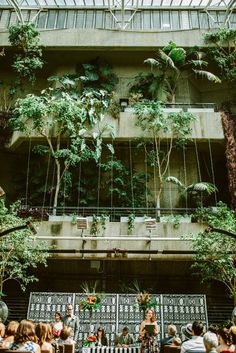 people sitting on benches in front of a building with plants hanging from it's sides