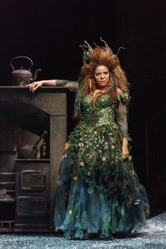 a woman in a green dress standing next to an old stove with leaves on it