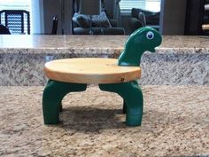 a green toy turtle sitting on top of a wooden bench in front of a kitchen counter