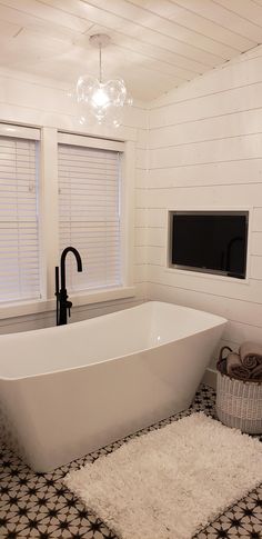 a white bath tub sitting in a bathroom next to two windows and a rug on the floor