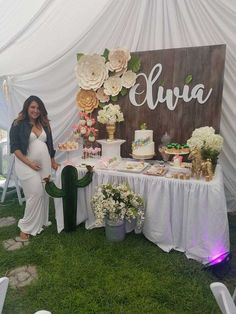 a pregnant woman standing next to a table filled with cake and desserts at a baby shower