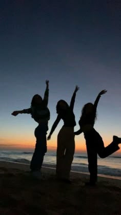 three people standing on the beach with their arms in the air and one person jumping up