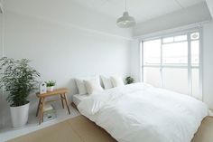 a white bed sitting under a window next to a wooden table with a potted plant on it