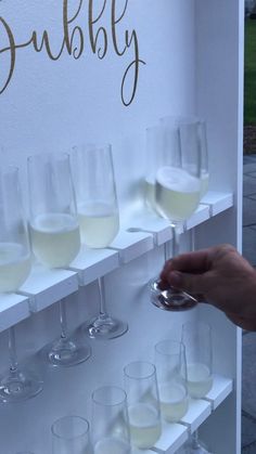 a person is holding a wine glass in front of several glasses on a shelf that are filled with white wine