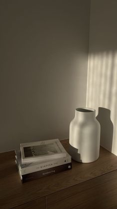 a white vase sitting on top of a wooden table next to a bookshelf