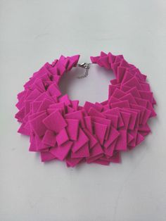 a pink necklace is shown on a white surface and has many small pieces of fabric in the shape of squares