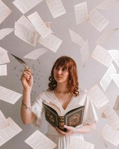 a woman holding a book while surrounded by books flying in the air above her head