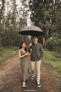 a man and woman walking down a dirt road holding an umbrella