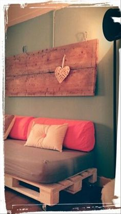 a bed made out of pallets with a heart hanging on the wall above it