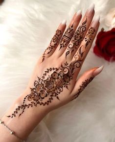 a woman's hand with henna tattoos on it and flowers in the background