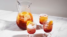 three glasses and pitcher filled with drinks on a marble counter top next to each other