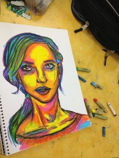 a drawing of a woman's face with colored pencils on the table next to it