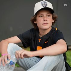 a young boy sitting on the ground holding a water bottle