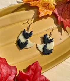 two earrings with black and white designs on them sitting next to autumn leaves, which are laying on a yellow platter