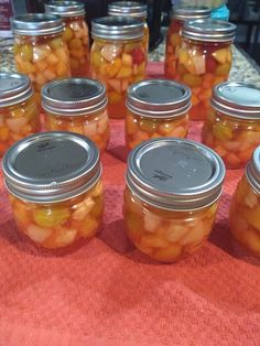 several jars filled with pickles sitting on top of a red cloth covered tablecloth