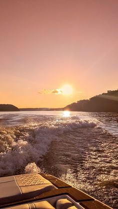 the sun is setting over the water from a boat in the ocean, with waves coming up to shore