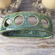 a green vase sitting on top of a wooden table next to some rocks and candles