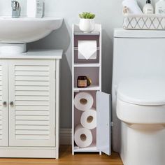 a white toilet sitting next to a sink and a cabinet with rolls of toilet paper on it