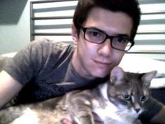 a man in glasses holding a cat on his chest and smiling at the camera while laying down