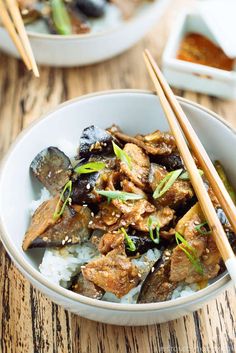 a white bowl filled with meat and rice next to chopsticks on top of a wooden table