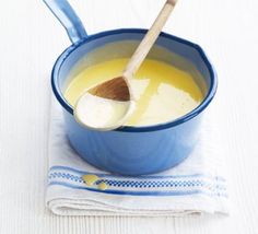 a blue bowl filled with yellow liquid and a wooden spoon on top of a white cloth