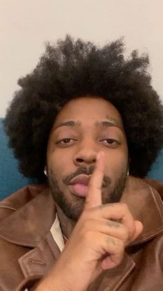 a man with an afro is making a finger sign while sitting on a blue couch