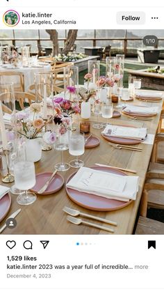 the table is set with pink and white plates, place settings, and vases