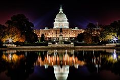 the capitol building lit up at night with lights reflecting in the water and trees around it