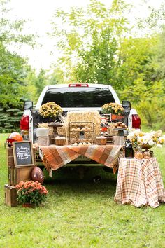 a truck with hay and pumpkins in the back is parked on grass next to a picnic table