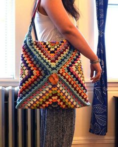 a woman holding a multicolored crocheted bag in front of a window