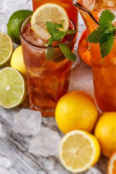 two glasses filled with lemonade and limes next to sliced lemons on ice