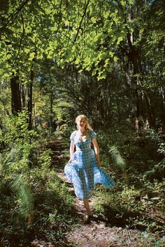 a woman in a blue dress is walking through the woods