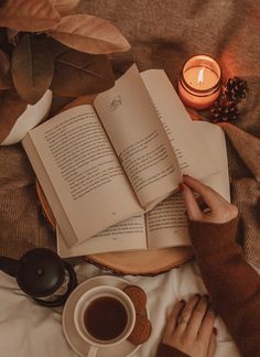 a person reading a book next to a cup of coffee and an open book on a bed