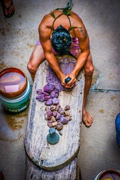 a man sitting on top of a wooden table covered in purple rocks and pebbles next to paint cans