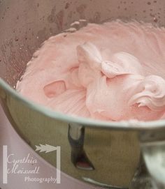 a metal bowl filled with pink icing on top of a counter