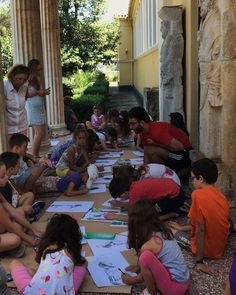 a group of children sitting on the ground doing arts and crafts in front of an old building