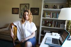 a woman sitting on a chair in front of a desk with a laptop and lamp