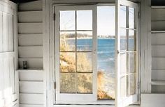 an open window on the side of a white house with water in the background and grass growing outside