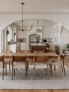 a dining room table and chairs in front of a kitchen with an archway leading to the living room