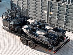 two vehicles with bicycles on the back are parked in front of a shipping container that is attached to a flatbed trailer