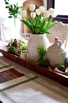 white tulips sit in a vase on a tray with other flowers and greenery