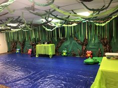 an indoor play area is decorated with green and blue plastic tarps, trees, and other decorations