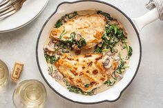 a skillet filled with chicken and spinach covered in gravy next to wine glasses