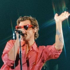 a man with sunglasses on his head singing into a microphone and holding up one hand