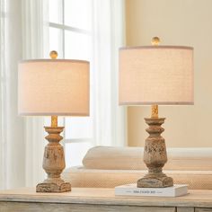 two lamps sitting on top of a table next to a book and lamp shade in front of a window