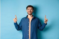 Skeptical young guy smirk and look doubtful, pointing fingers up upset, standing on blue background. Copy space Pointing Fingers, Blue Background, Puma Jacket, Rain Jacket, Athletic Jacket, Blue