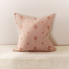 a pink pillow sitting on top of a bed next to a white wall and floor