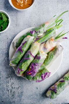 spring rolls on a plate with dipping sauces and green leafy vegetables next to them