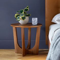 a small table with a plant on it next to a bed