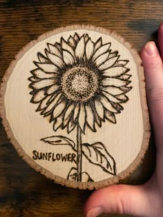 a hand holding a wooden coaster with a sunflower on it